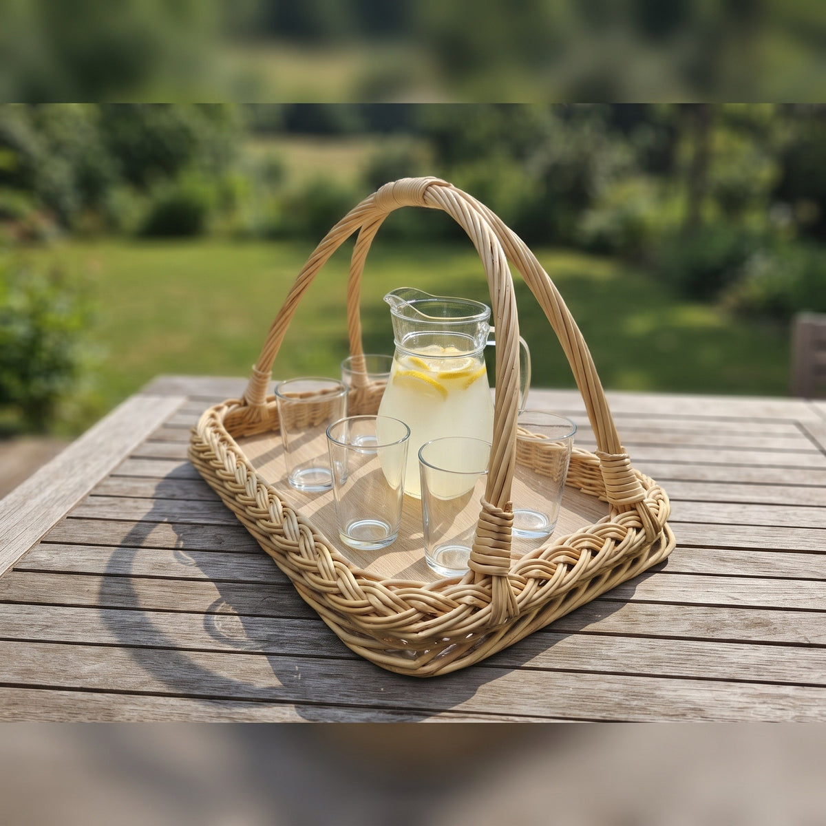 Vytelių padėklas su rankenomis ant medinio sodo stalo, ant jo stiklinis ąsotis limonado ir stiklinės