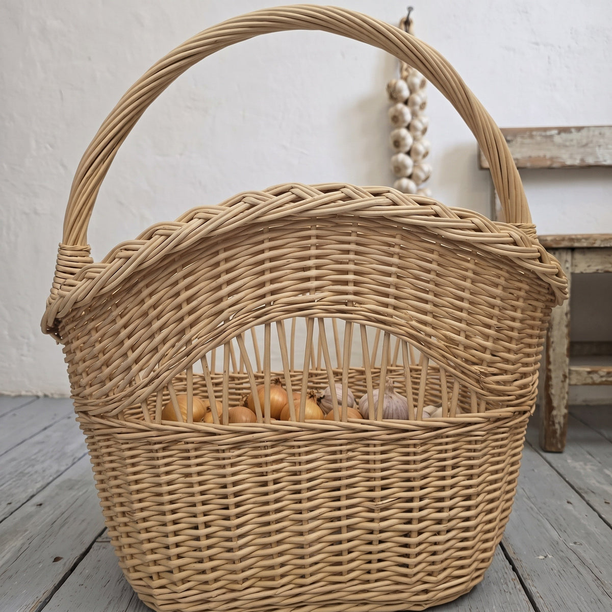 Aukšta pintinė su rankena, už ažūrinės juostos matyti svogūnai, šalia medinė kėdutė