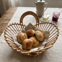 Runde Obstschale aus Weide mit zwei Schlaufenhenkeln als Brotkorb für Brötchen auf einem Leinentuch am Frühstückstisch