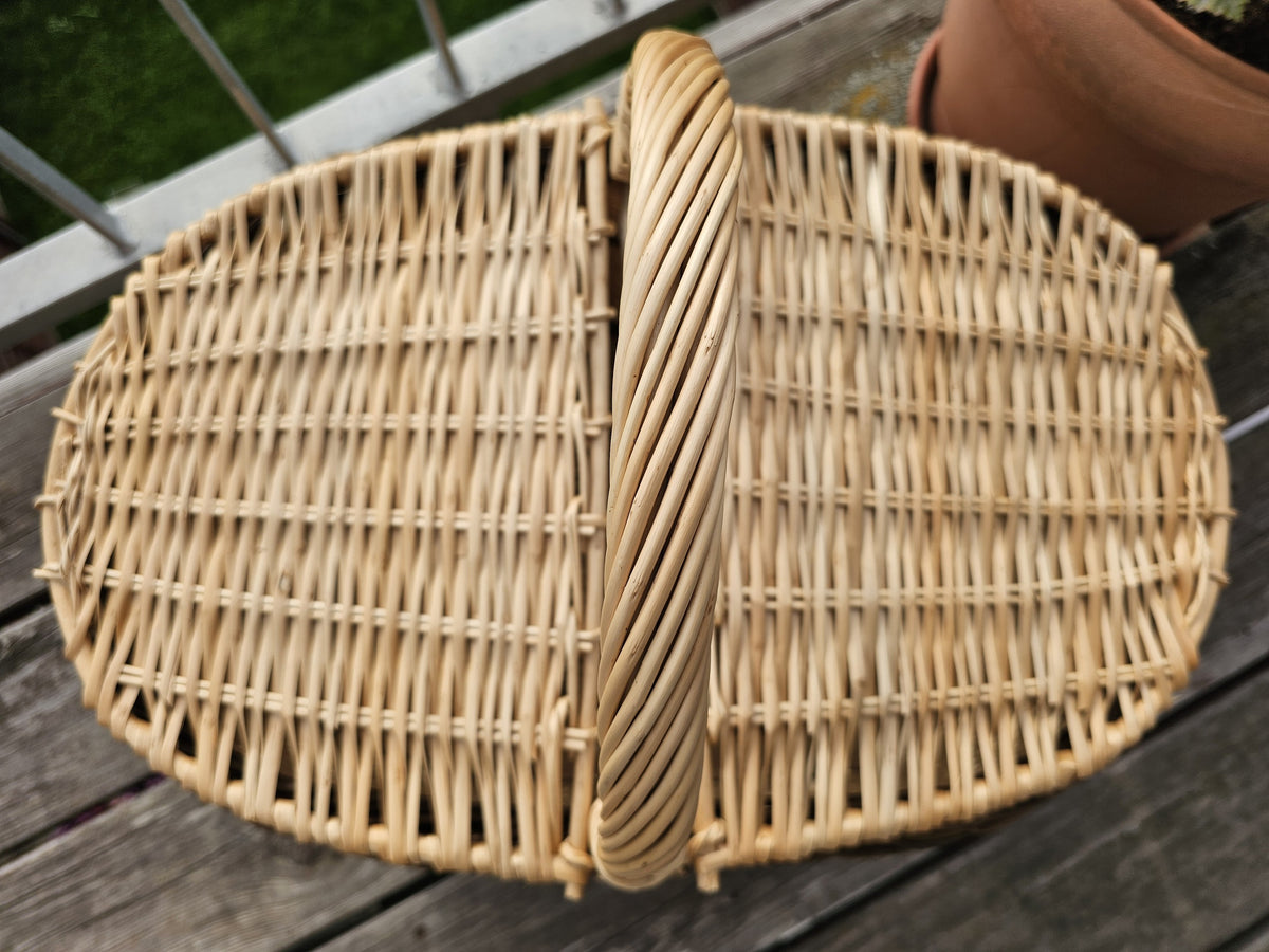 Ovali pikniko pintinė iš viršaus: du uždaryti pinti dangčiai ir rankena tarp jų