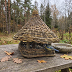 Vytelių lesykla su pintu stogeliu ir kvadratiniu padėklu ant sodo stalo tarp rudens lapų, mėlynoji zylė lesa sėklas