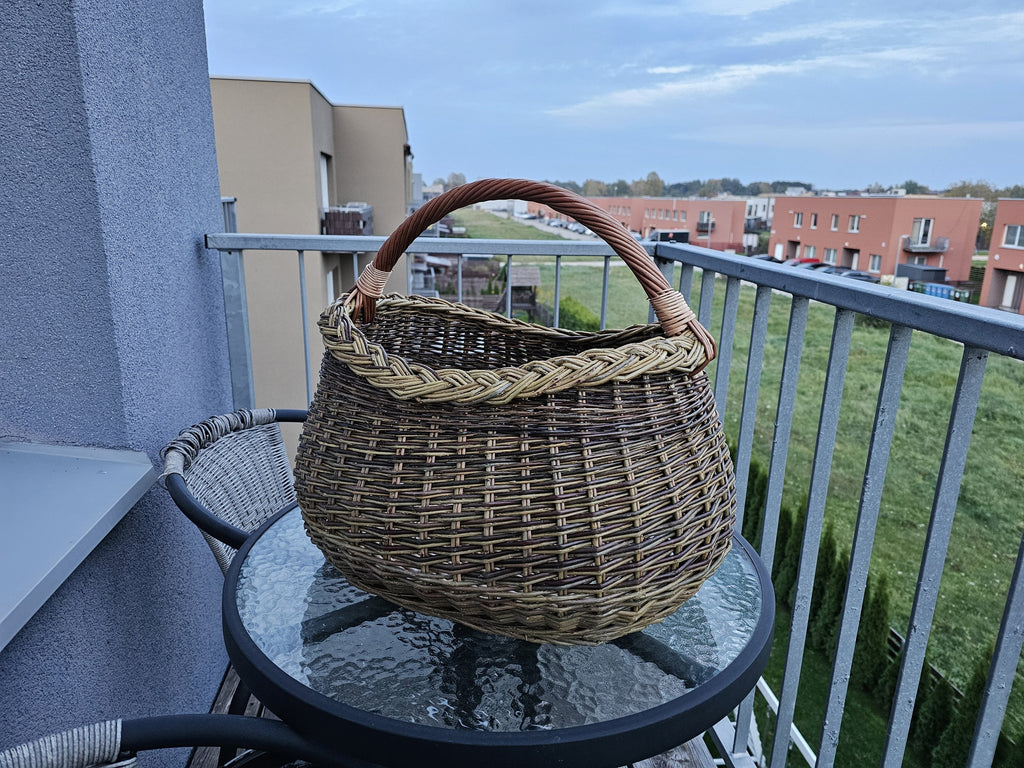 Grybavimo pintinė kasele pintu kraštu ant apvalaus stiklinio staliuko miesto balkone, už jos daugiabučiai