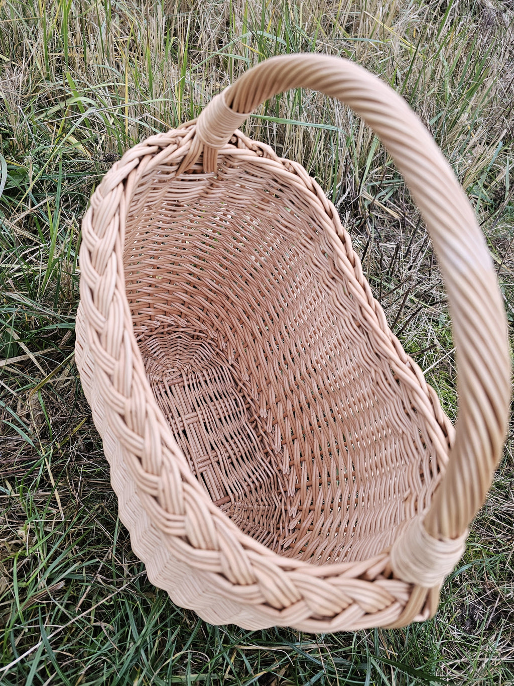 Tuščia pintinė žolėje iš arti: storas pintas kraštas ir plati lenkta rankena