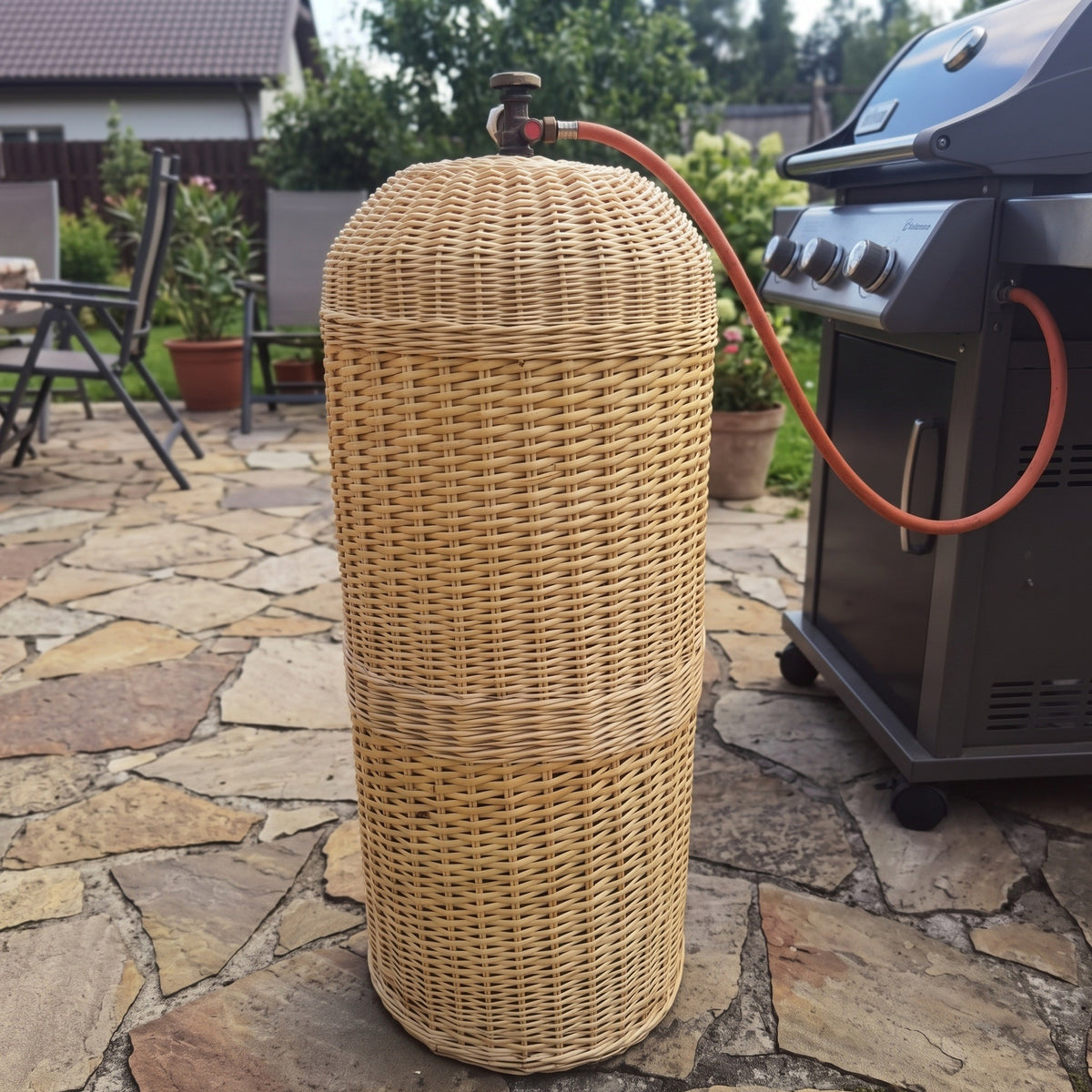 Aukštas pintas gaubtas ant akmeninės terasos prie kepsninės: ventilis ir žarna išeina pro angą viršuje