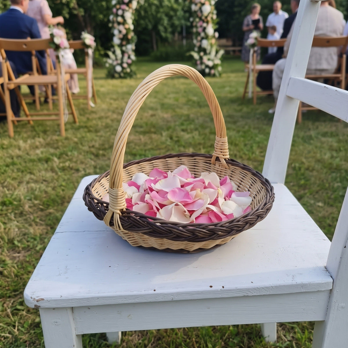 Pintinė su aukšta rankena, pilna rožių žiedlapių, ant baltos kėdės vestuvių ceremonijoje sode
