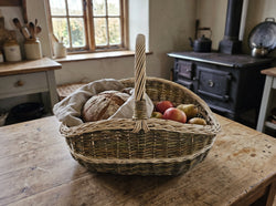 Handwoven wicker market basket with a twisted handle holding bread wrapped in linen, apples and pears on a farmhouse kitchen table