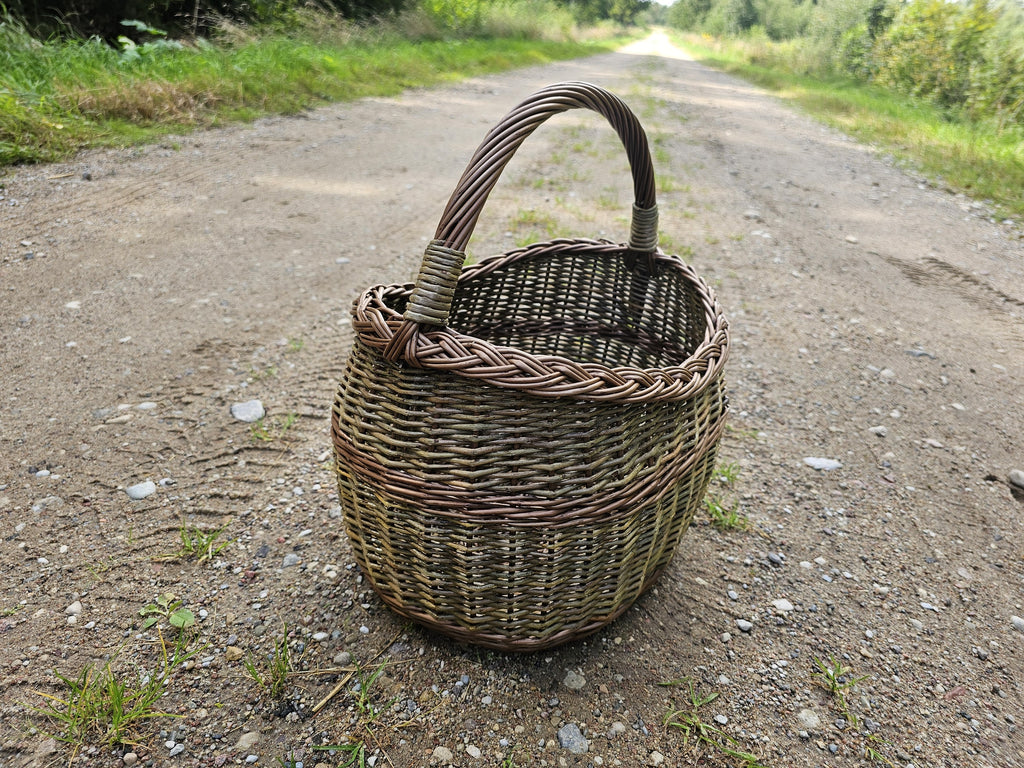 Pintinė ant kaimo žvyrkelio, už jos tolsta kelias, šoninė šviesa apšviečia pynimą