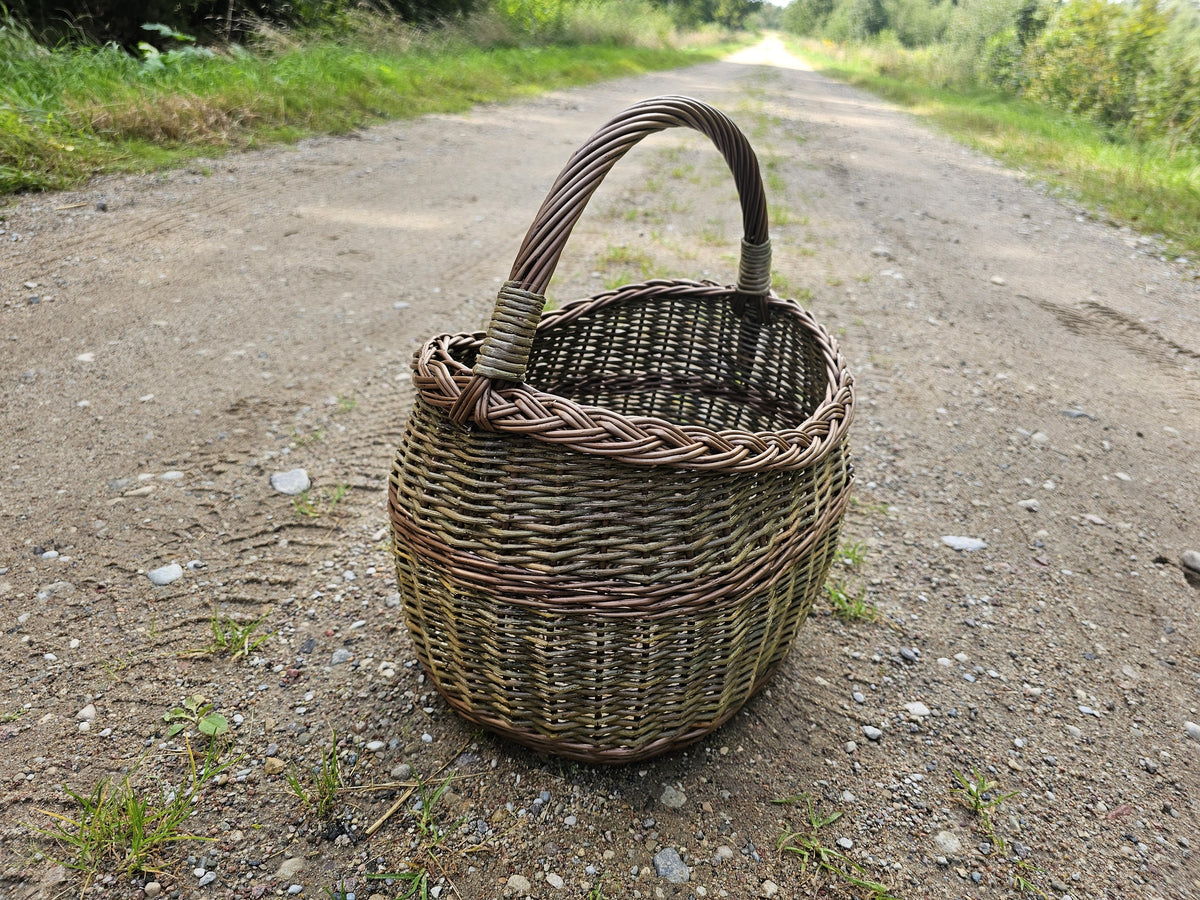 Pintinė ant kaimo žvyrkelio, už jos tolsta kelias, šoninė šviesa apšviečia pynimą