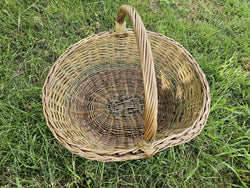 Top view of the large oval willow basket on the grass, showing the woven base, twisted rim and the tall twisted handle