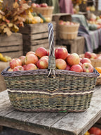 Large wicker market carrier with twisted handle heaped with red apples on a rustic table at an autumn farmers market