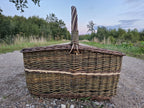 Side view of the large willow firewood basket with its tall upright handle on a gravel road under an evening sky