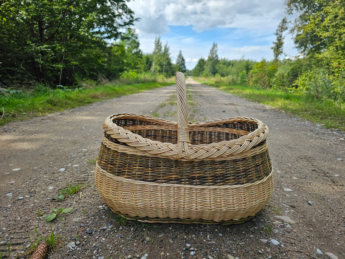 Turgaus pintinė iš priekio žvyro keliuke: lanko formos rankena kyla iš kasele pinto krašto