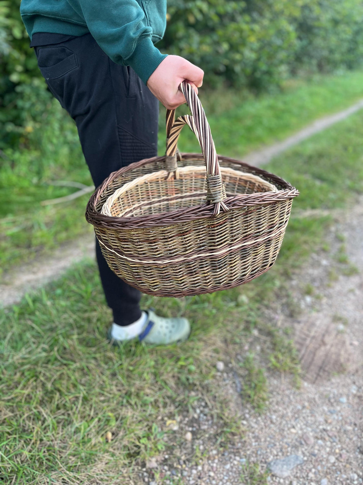 Žmogus neša sudėtas pintines už susuktos rankenos kaimo keliuku – matyti jų dydis