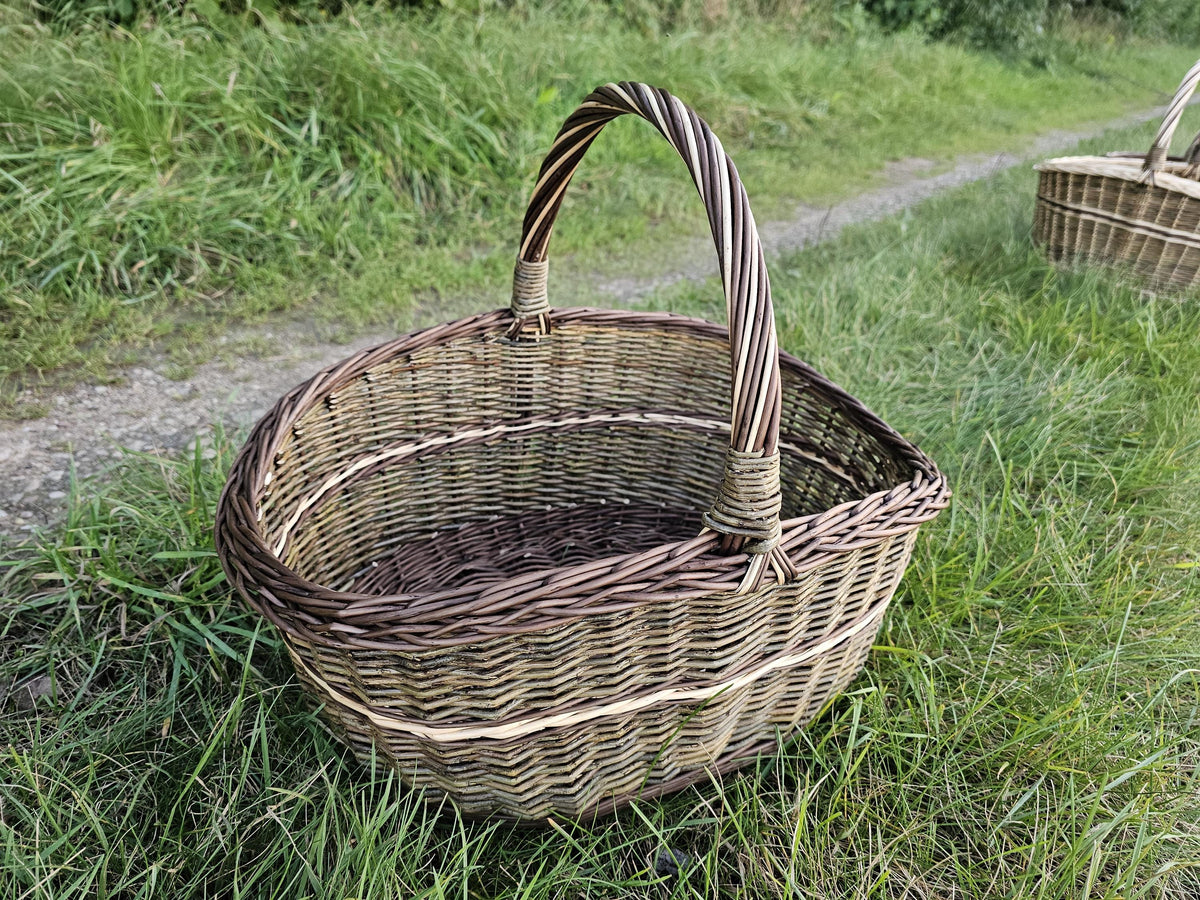 Turgaus pintinė su susukta rankena ir platėjančiais šonais ant žolės, už jos ant tako kita pintinė