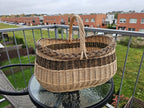 Large oval willow basket with braided rim on a round glass table on a balcony