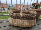 Large oval willow basket on a wooden balcony table beside a flower pot