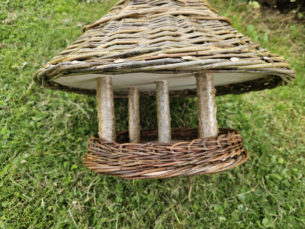 Iš arti: stulpeliai iš šakų laiko pintą stogelį virš medinio padėklo su storu pintu kraštu