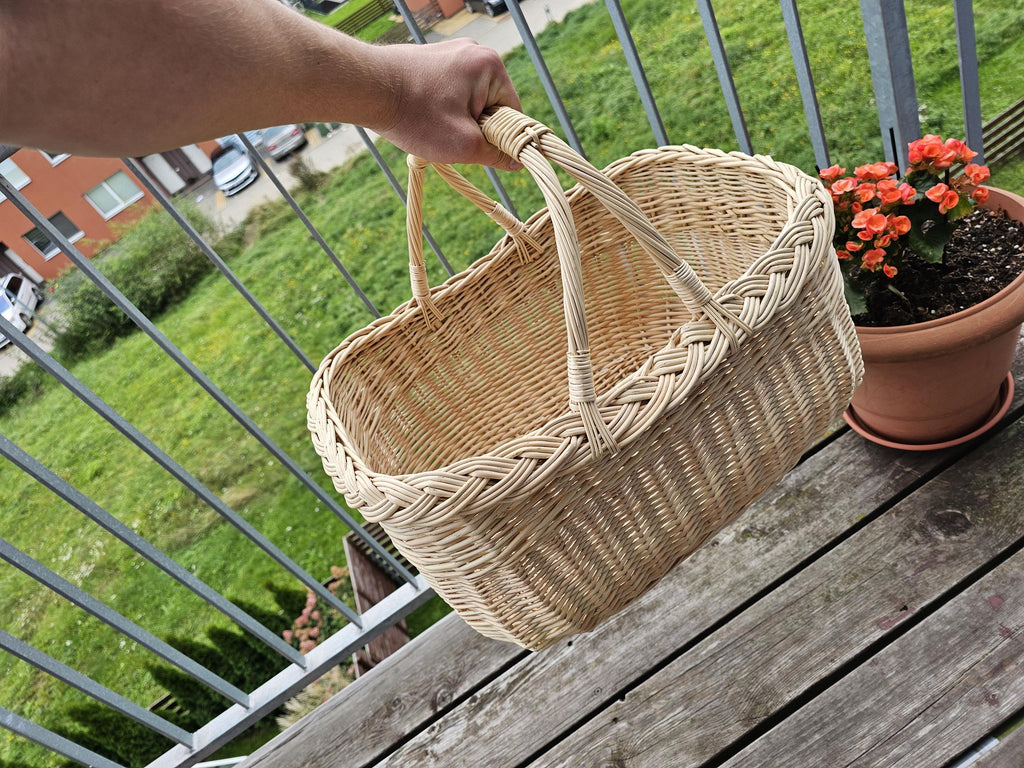 Ranka neša didelę ovalią pintinę už sujungtų rankenų balkone – matyti jos dydis ir gylis