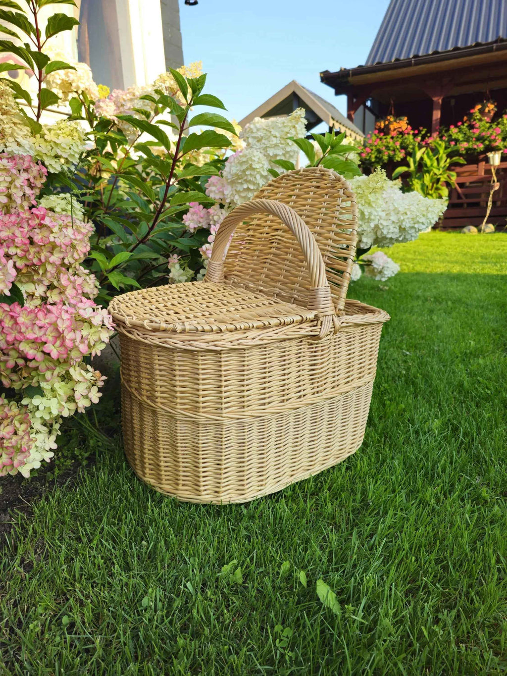 Ovali pikniko pintinė su lanko formos rankena, dangtis praviras, matyti pynimas viduje